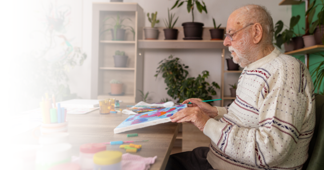 Elderly man painting at a memory care facility, engaging in a dementia-friendly activity.