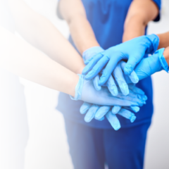 Nurses in blue scrubs stacking hands together to show teamwork and support for Nurses Week